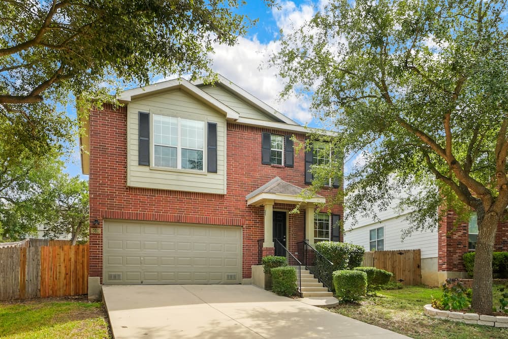 Traditional brick two-story house with a prominent garage and mature trees, representing a home with a fortified roof and the necessity of regular inspection and maintenance to withstand weather in Louisiana.