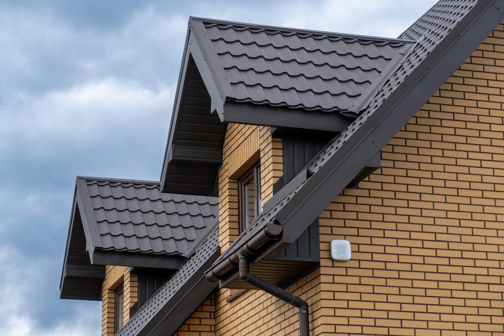 Dark brown stamped metal roof with matching gutters installed on a yellow brick house.